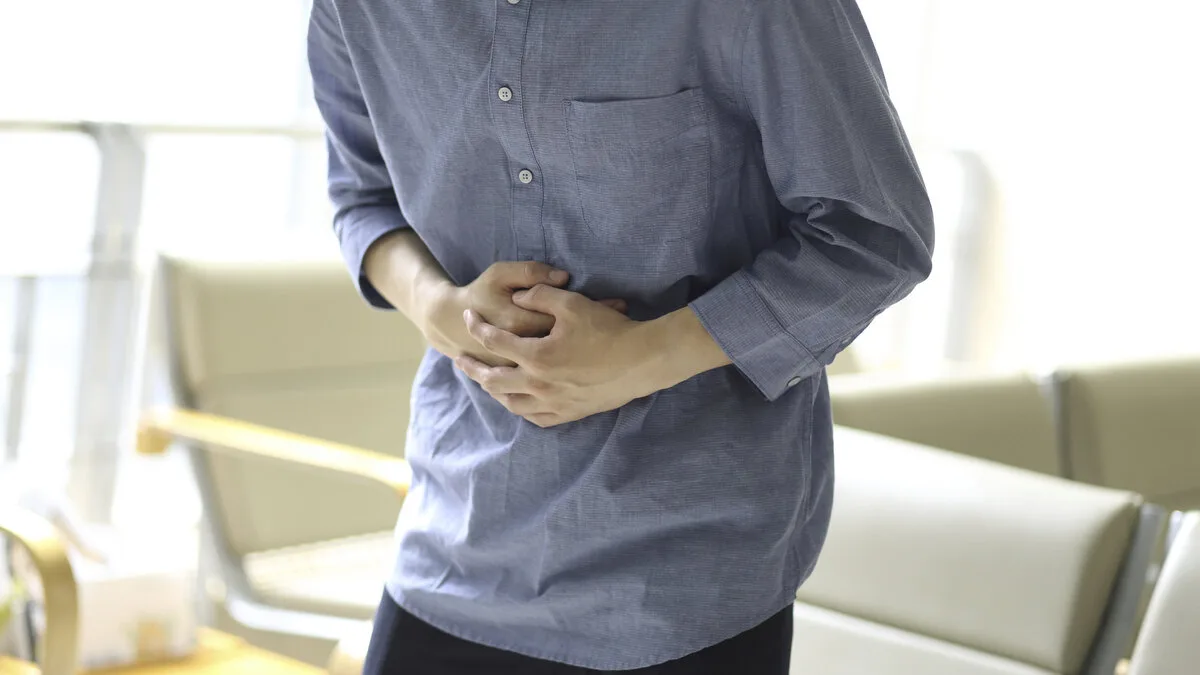 복통으로 배를 감싸 쥔 남성의 상반신