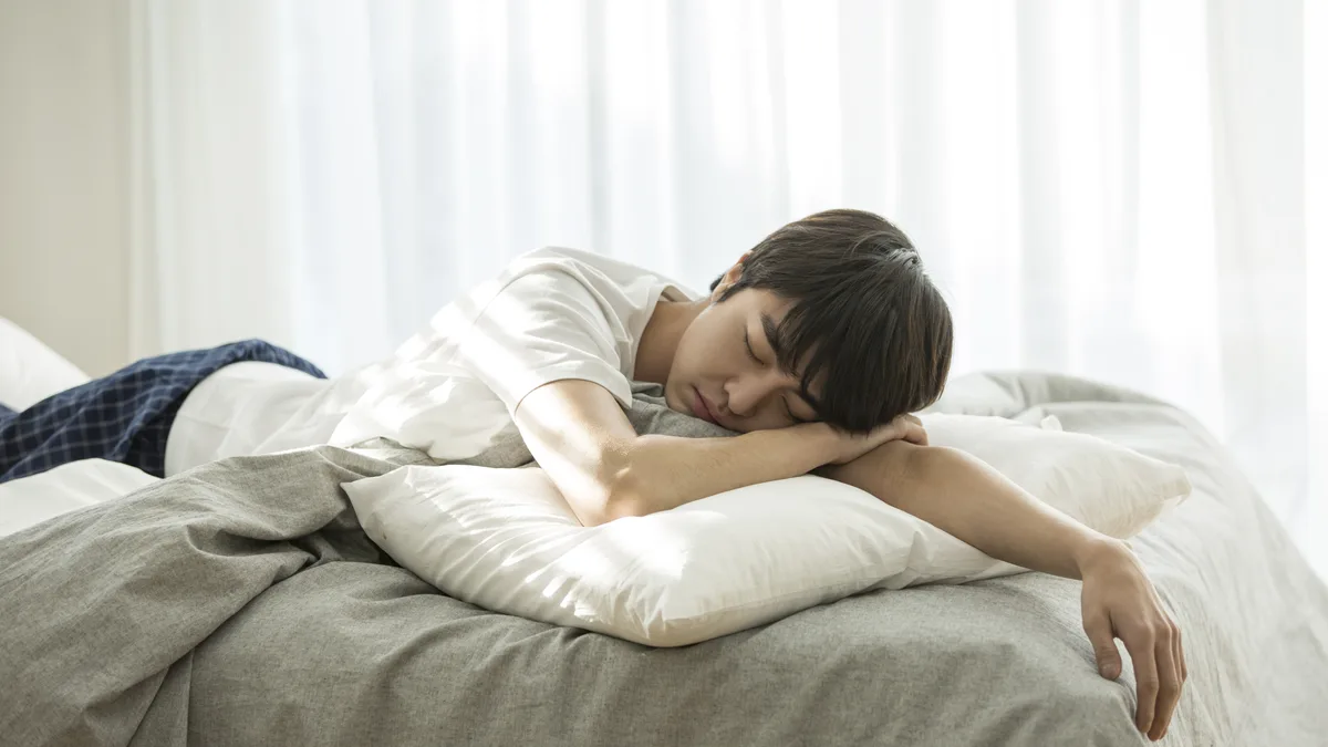 침구가 정돈된 침대에 엎드려 잠든 남성의 모습