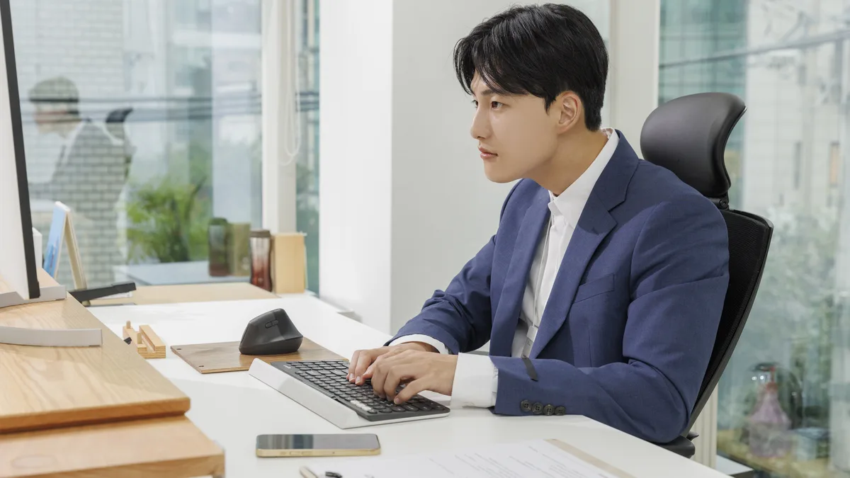 창이 있는 사무실 책상에서 컴퓨터로 실내 근무 중인 직장인